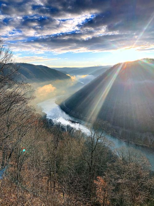 A scenic view of a river winding through mountains, with sunlight breaking through clouds and illuminating the landscape.