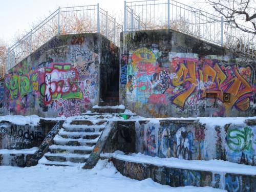 Colorful graffiti covers a concrete wall and staircase, surrounded by snow in a winter setting.
