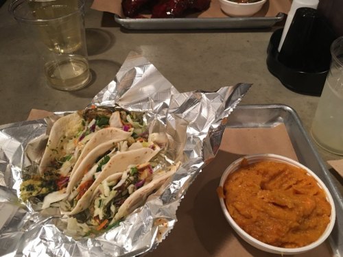 A plate with three tacos wrapped in foil, accompanied by a side of orange sweet potato mash.