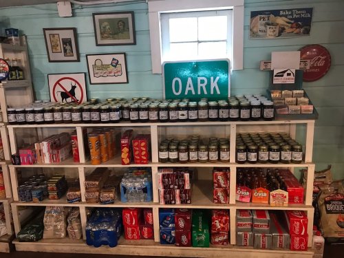 A rustic store shelf filled with jars, snacks, and beverages, with a green "Oark" sign in the background.