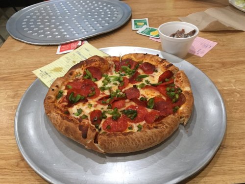 A pepperoni pizza with green peppers on a metal tray, accompanied by a small cup of dipping sauce.