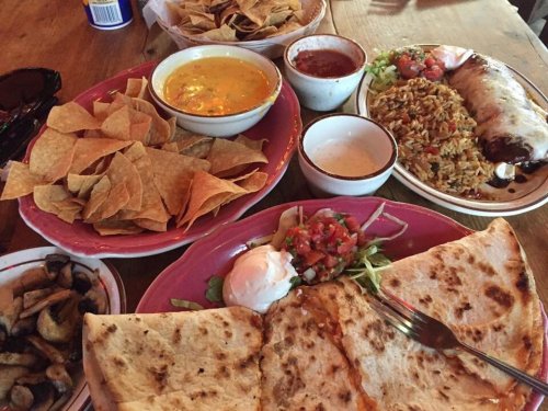 A spread of Mexican food featuring chips, queso, rice, salsa, a burrito, and a large quesadilla on a wooden table.