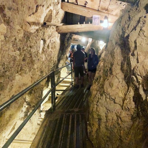 Visitors explore a narrow, rocky passageway with wooden supports and railings inside a cave.