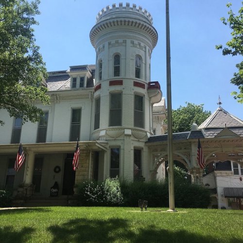 Historic white mansion with a tower, surrounded by greenery and American flags, under a clear blue sky.