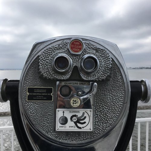 A coin-operated binocular viewer overlooking a body of water under a cloudy sky.