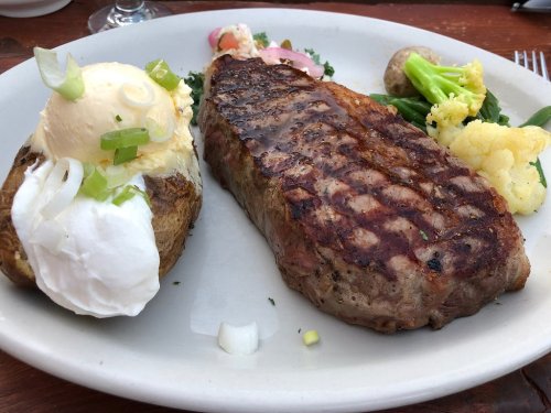 A grilled steak served with a baked potato topped with sour cream and green onions, alongside mixed vegetables.