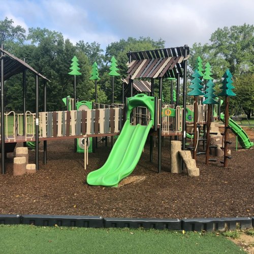 Colorful playground with a green slide, wooden structures, and tree-shaped decorations on a mulch surface.