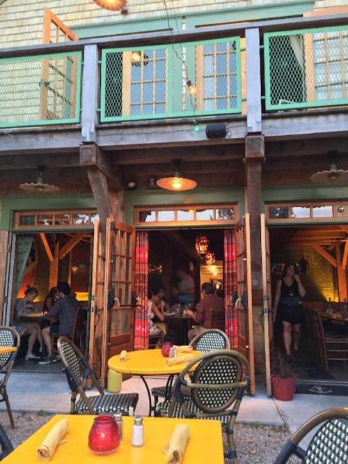 A cozy restaurant with outdoor seating, warm lighting, and patrons enjoying their meals inside and outside.