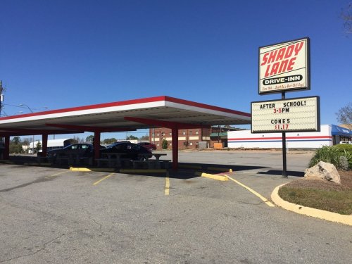 A drive-in restaurant with a sign reading "Shady Lane" and a message about after-school hours and ice cream cones.