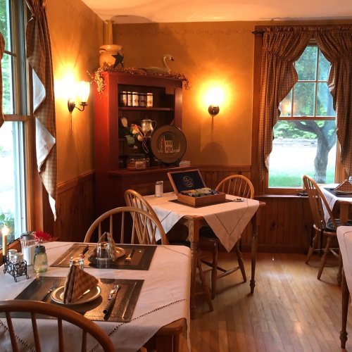 Cozy dining area with wooden chairs, tables set with linens, and warm lighting from wall sconces.