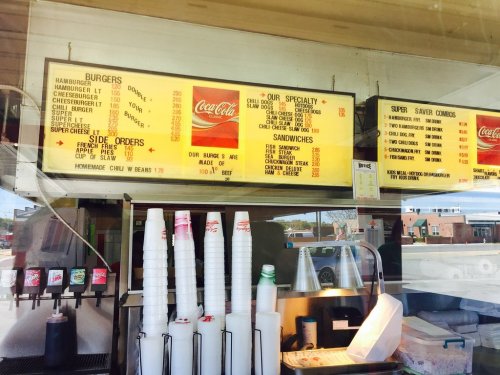 Menu board displaying burgers, sandwiches, and sides at a fast-food restaurant, with prices and Coca-Cola branding.
