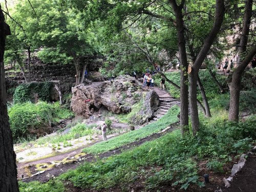 A lush, green landscape with rocky formations and a winding path, where people are exploring the natural surroundings.