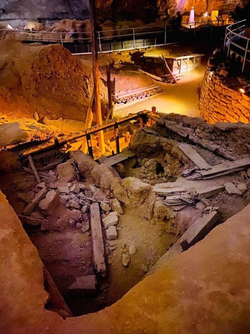 An underground excavation site with rocky terrain, wooden supports, and warm lighting illuminating the area.