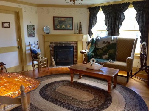 Cozy living room with a fireplace, patterned rug, wooden furniture, and decorative items on the walls.