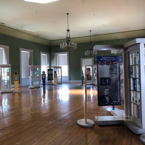 A spacious museum room with wooden floors, featuring display cases and informational panels under soft lighting.