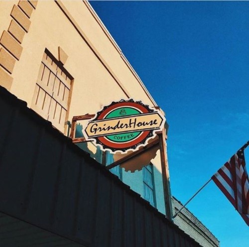 Sign for GrinderHouse Coffee against a clear blue sky, with an American flag visible in the background.
