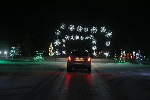 A car drives through a festive display of colorful holiday lights and snowflake decorations at night.