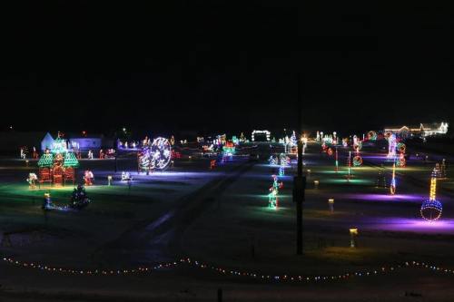 A festive display of colorful holiday lights illuminating a snowy landscape at night.