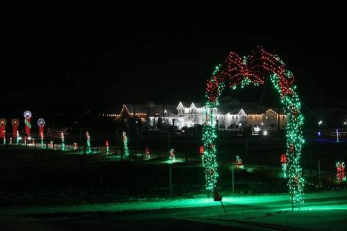 A festive display of colorful Christmas lights at night, featuring arches and decorations in a snowy landscape.