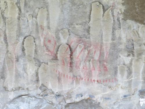 Ancient rock art featuring red symbols and figures on a textured stone surface.