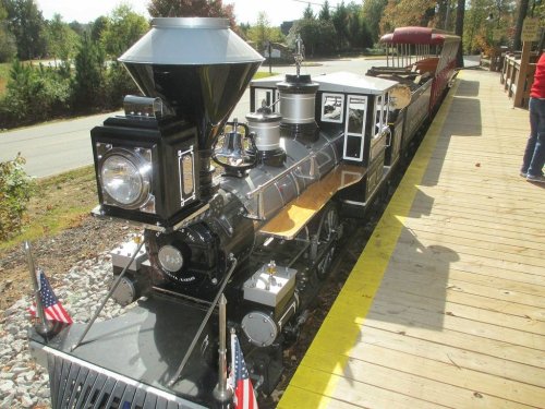 A vintage steam locomotive with a black and silver exterior, parked on a wooden platform with American flags.