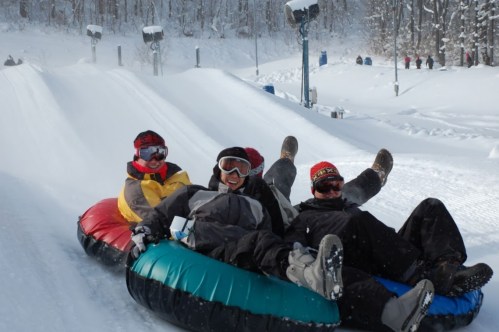 Three people enjoying a snow tubing ride down a snowy slope, smiling and wearing winter gear.