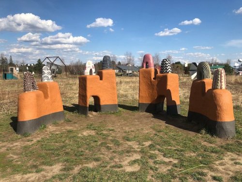 Colorful, abstract sculptures resembling hills or structures in a grassy field under a blue sky with clouds.