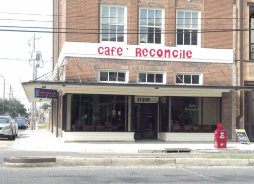 Exterior of Café Reconcile, a brick building with large windows and a sign above the entrance, located on a city street.