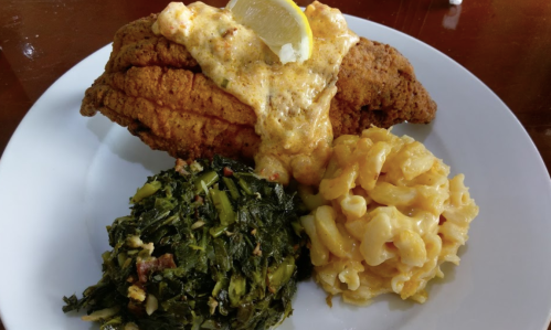 A plate featuring fried catfish topped with sauce, served with macaroni and cheese and sautéed greens.