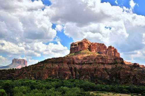 A rocky plateau rises against a backdrop of blue sky and fluffy clouds, surrounded by green vegetation.