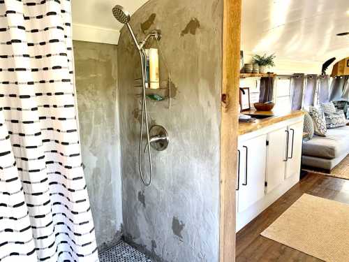 A modern shower area with a concrete wall, a showerhead, and a patterned curtain, leading to a cozy living space.