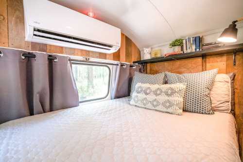 Cozy bedroom in a tiny home with a bed, decorative pillows, a window, and a wall-mounted air conditioner.