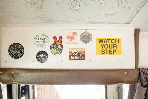 A collection of colorful stickers on a wall, including logos for breweries and a caution sign that says "WATCH YOUR STEP."