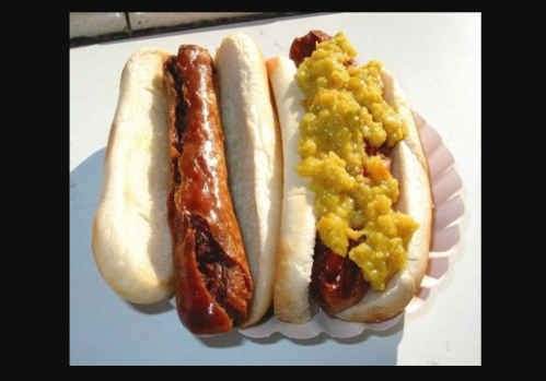 Two hot dogs in buns, one plain and the other topped with a yellow-green condiment.