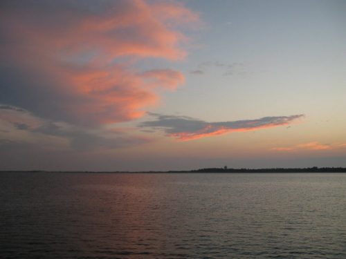 A serene sunset over calm waters, with soft pink clouds reflecting in the sky.