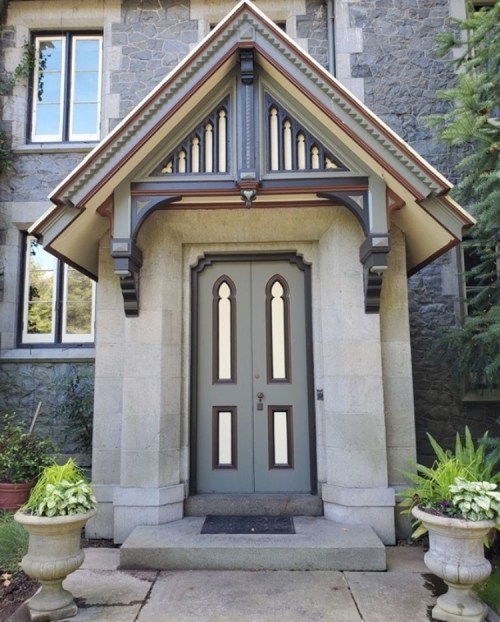 A decorative entrance with a double door, stone walls, and ornate roof details, flanked by potted plants.