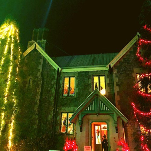 A stone house decorated with colorful Christmas lights at night, featuring a welcoming entrance and festive atmosphere.