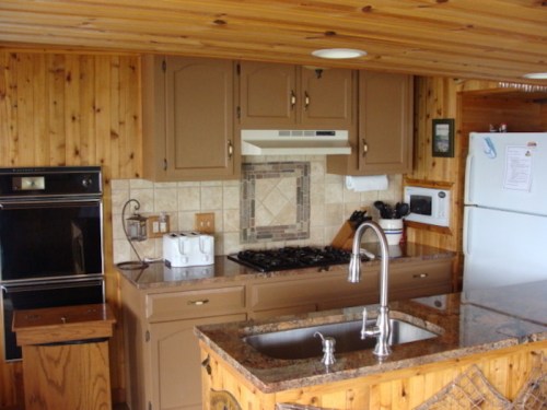 A cozy kitchen with wooden walls, a gas stove, oven, and a granite countertop with a sink.