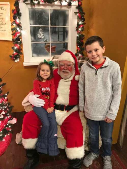 A young girl and boy pose with Santa Claus in a cozy, festive setting with holiday decorations.