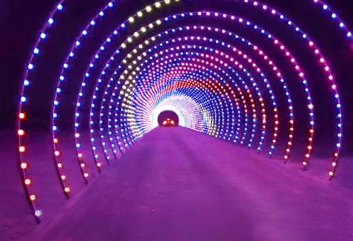 A colorful illuminated tunnel with vibrant lights in a spiral pattern, leading into darkness.