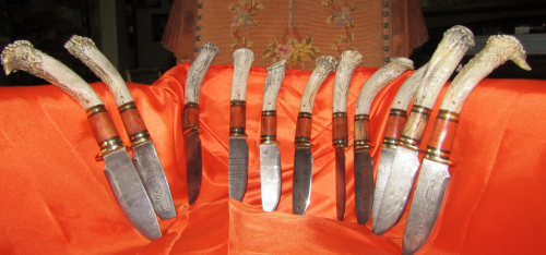 A collection of ornate knives with antler handles displayed on an orange fabric background.