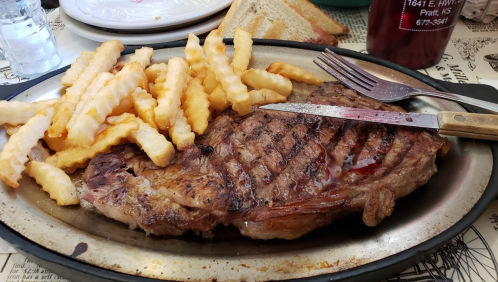 A sizzling steak on a metal plate, accompanied by golden crinkle-cut fries and a knife and fork.