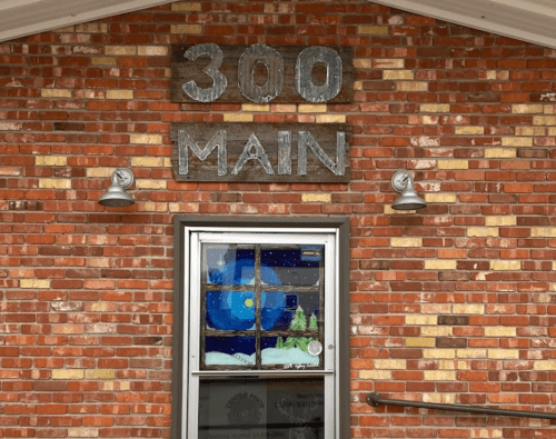 Brick building facade with a sign reading "300 MAIN" above a window featuring a winter scene.