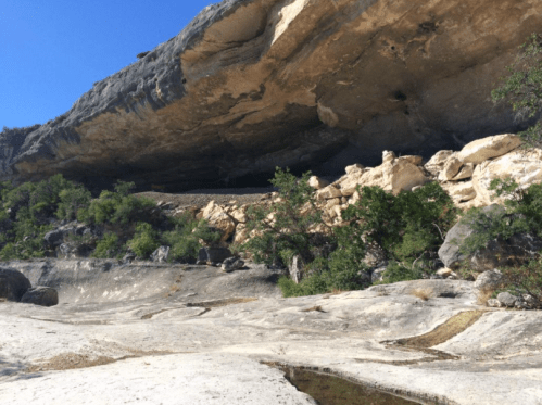 A rocky overhang with lush greenery below, set against a clear blue sky.