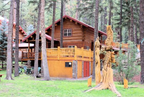 A rustic log cabin surrounded by tall trees, featuring a wooden deck and a carved tree sculpture in the foreground.