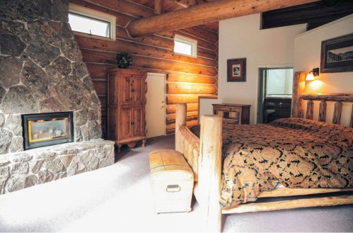 Cozy log cabin bedroom featuring a stone fireplace, wooden furniture, and warm, rustic decor.