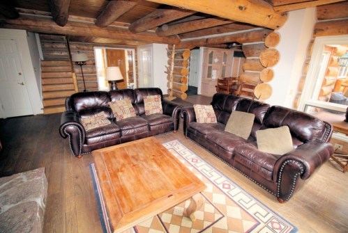 Cozy log cabin interior featuring brown leather sofas, a wooden coffee table, and rustic decor.