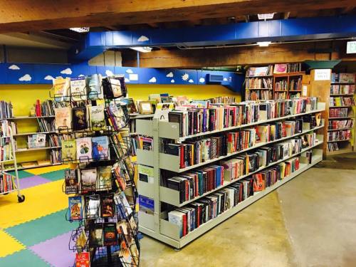 A cozy library interior featuring colorful walls, bookshelves filled with books, and a display rack of titles.