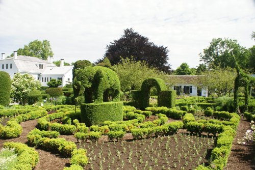 A lush garden featuring topiary elephants, neatly trimmed hedges, and vibrant greenery surrounding a white house.
