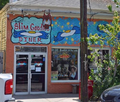 Colorful exterior of Slim Goodies Diner featuring a mural and an open sign, with a view of the interior through the window.